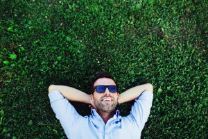 Portrait of a young happy man relaxing on the grass with his hands under the head