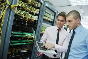 two men looking at a laptop while assessing a server